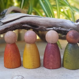 Puede incluir: Cuatro muñecos de madera con caras pintadas y cuerpos de diferentes colores. Los muñecos están de pie sobre una superficie de madera. Los muñecos están pintados en tonos de naranja, amarillo, rojo y verde.