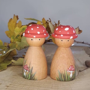 Peut inclure: Deux figurines de champignons en bois avec des chapeaux peints en rouge et blanc et des corps bruns. Chaque figurine a un petit champignon peint sur le devant.