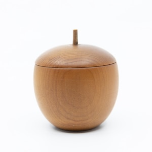 Peut inclure: Un récipient en bois en forme de gland avec un couvercle et une petite tige. Le récipient est en bois brun clair et repose sur un fond blanc. Le couvercle s'adapte parfaitement au récipient, créant un aspect lisse et homogène. Idéal pour ranger de petits objets.