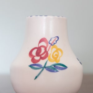 Puede incluir: Una jarra de cerámica blanca con un borde azul y un diseño floral con flores rojas, amarillas y verdes.