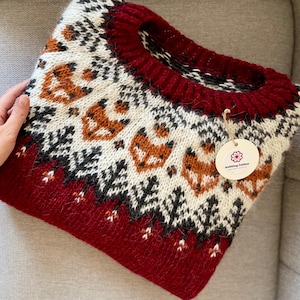 Folded red Icelandic wool sweater with apricot fox and forest yoke pattern