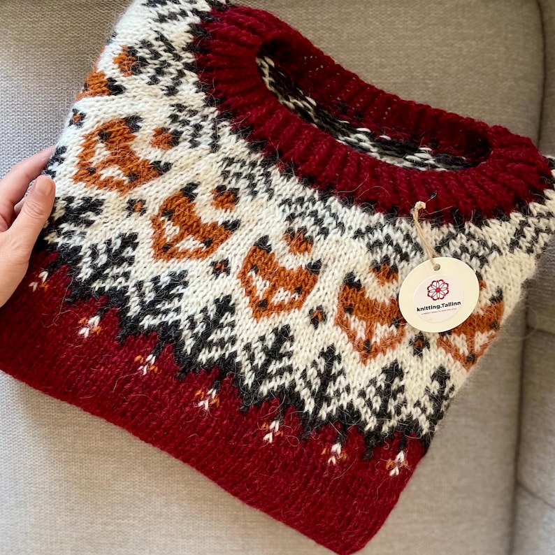 Folded red Icelandic wool sweater with apricot fox and forest yoke pattern