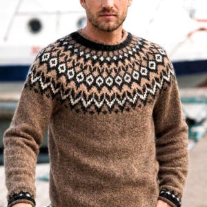 May include: A long-sleeved knit sweater in a solid brown color featuring a circular yoke pattern. The yoke displays a geometric design in black, white, and tan colors. The sweater has a round neckline and matching geometric patterns on the cuffs.
