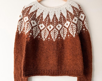 May include: A long-sleeve knit sweater featuring a solid rust-colored body and a round neckline. The yoke displays a contrasting white and rust-colored geometric leaf pattern. The cuffs also feature a small white geometric detail.