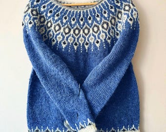 Può includere: Un maglione blu lavorato a maglia con un motivo a girocollo. Il girocollo presenta un design geometrico in bianco, nero e grigio. Il maglione ha maniche lunghe e girocollo. I polsini e l'orlo sono rifiniti con un bordo bianco e grigio.
