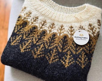 May include: A long-sleeve knit sweater featuring a cream-colored ribbed neckline and a gradient pattern of golden-brown and dark charcoal gray tree motifs. A round white tag attached to the collar displays the text Knitting.Tallinn.