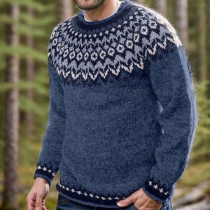 May include: A long-sleeved crew neck sweater in a heathered blue knit. The garment features a decorative yoke and cuffs with a repeating geometric pattern in shades of dark blue, light gray, and white, creating a textured appearance.