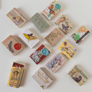 May include: Assortment of small, decorative matchboxes with various designs and patterns. The matchboxes feature a variety of themes, including floral, animal, and abstract designs. Some matchboxes have text on them, such as "Boric Acid" and "Eau De Cologne".