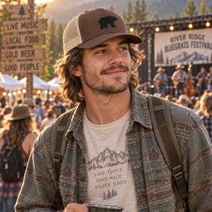 May include: A brown and tan trucker hat with a black bear silhouette, a beige t-shirt with a mountain graphic and the text "GOOD PEOPLE GOOD MUSIC WILDER PLACES", and a dark green metal mug with the text "Music Brings Us Closer".
