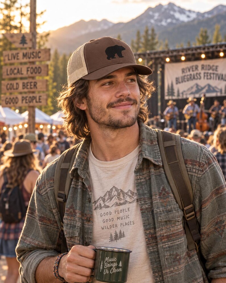 May include: A brown and tan trucker hat with a black bear silhouette, a beige t-shirt with a mountain graphic and the text "GOOD PEOPLE GOOD MUSIC WILDER PLACES", and a dark green metal mug with the text "Music Brings Us Closer".