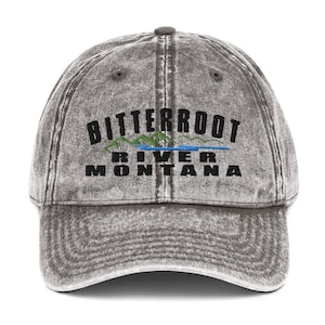May include: A grey distressed denim baseball cap with black embroidered text that reads "Bitterroot River Montana". The text is arched and the word "River" is centred below the word "Bitterroot".