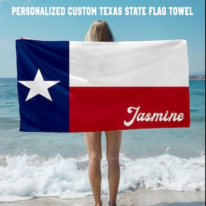 Puede incluir: Una toalla de playa con la bandera del estado de Texas con una estrella blanca sobre un fondo azul, una franja roja y una franja blanca. El nombre "Jasmine" está escrito en cursiva blanca en la franja roja.