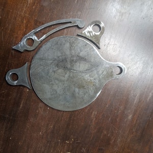 May include: Three metal pieces, a round disc with a handle, a curved piece with a hole, and a small piece with a hole. The pieces are made of a silver metal and have a rough, unfinished look.
