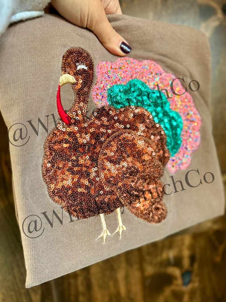 May include: A brown sweatshirt featuring a sequined turkey design. The turkey has a brown body, a red wattle, and a colorful tail with pink, green, and orange sequins. The text "@WhitchCo" is printed on the sweatshirt.
