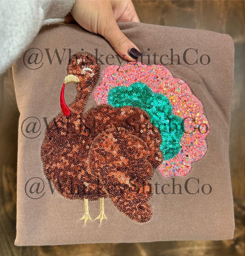 May include: A brown sweatshirt featuring a sequined turkey design. The turkey has a brown sequined body, a red wattle, and a colorful tail with pink, teal, and orange sequins. The sweatshirt has the text "@WhiskeyStitchCo" repeated.