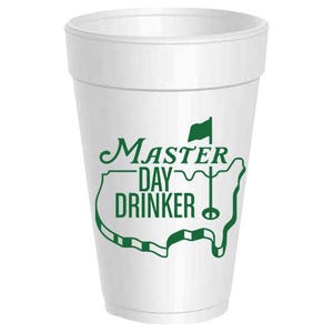 May include: A white foam cup with a green graphic that reads "Master Day Drinker." The design includes a golf flag and a stylized outline of the United States. The cup is designed for beverages.