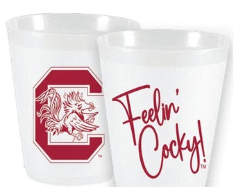 May include: Two white plastic cups. One cup features a maroon logo of a stylized rooster inside a maroon letter C. The other cup has the words "Feelin' Cocky!" in maroon script.