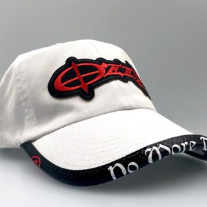 May include: A white baseball cap with a curved brim. The cap features a red and black logo on the front and the words "No More Tears" in white on the brim. The cap is made of a soft material.