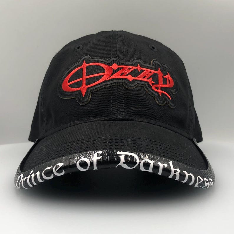 May include: Black baseball cap featuring the name "Ozzy" in red embroidered lettering. The brim of the cap displays the text "Prince of Darkness" in white script. The cap is made of a durable fabric.