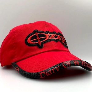 May include: Red baseball cap with a curved brim. The cap features the word "Ozzy" in black and red embroidery on the front. The brim has the words "Diary of a Madman" in red.