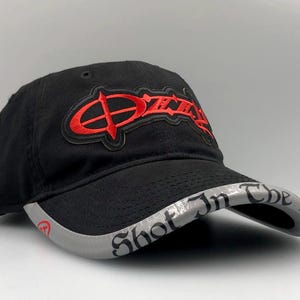 May include: Black baseball cap with the word "Ozzy" in red embroidered lettering. The brim is gray with the words "Shot In The Dark" in black lettering. A stylish accessory.