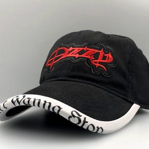May include: Black baseball cap with a curved brim. The cap features red embroidered text that reads "Ozzy" on the front and "Wanna Stop" on the brim. The cap is made of a durable fabric and has a classic, adjustable design.