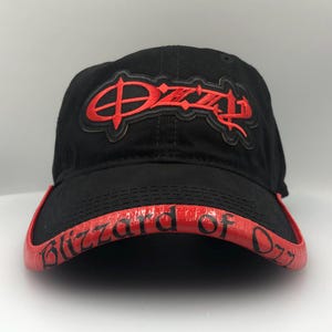 May include: Black baseball cap with red embroidered "Ozzy" logo on the front. The brim is red with the words "Blizzard of Ozz" in red lettering. A classic, stylish accessory.
