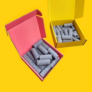 Puede incluir: Dos cajas de cartón abiertas, una rosa y otra amarilla, cada una llena de rodillos con patrones grises. Los rodillos están dispuestos en un patrón aleatorio.