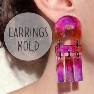 Puede incluir: Un par de pendientes de resina rosa y naranja con un diseño geométrico. Los pendientes tienen forma de arco con tres piezas rectangulares que cuelgan de la parte inferior. Los pendientes están hechos con resina transparente y tienen un efecto marmoleado.