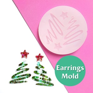 Puede incluir: Un molde de silicona rosa para hacer pendientes de árbol de Navidad. El molde tiene un diseño de espiral y dos formas de estrella. Se muestran dos pendientes terminados, hechos con resina de purpurina verde y roja.