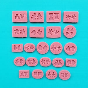 May include: A collection of pink silicone molds in various shapes, including snowflakes, flowers, trees, and abstract designs. The molds are arranged on a light blue surface, offering a variety of options for crafting or baking projects.
