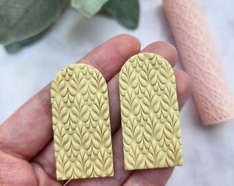 May include: Two yellow arch-shaped polymer clay earrings with a raised leaf pattern.