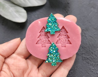 May include: A pink silicone mould with three Christmas tree shapes. Two of the shapes are filled with teal glitter.