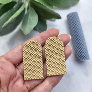 May include: Two beige, textured, arched, resin earrings. The earrings have a honeycomb pattern.