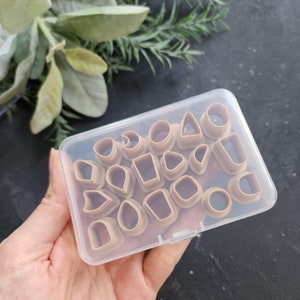 Könnte beinhalten: Eine transparente Plastik-Aufbewahrungsbox gefüllt mit verschiedenen braunen Plastikformen. Die Formen sind in verschiedenen Größen und umfassen Kreise, Quadrate, Dreiecke und andere geometrische Formen.