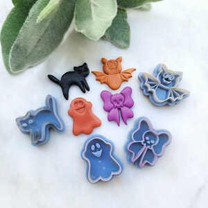 Könnte beinhalten: Ein Set mit acht Halloween-förmigen Ausstechern. Die Ausstecher sind aus blauem, violettem, orangefarbenem und schwarzem Kunststoff. Die Ausstecher sind in Form eines Geistes, einer Fledermaus, einer Katze, einer Schleife und eines Schädels.