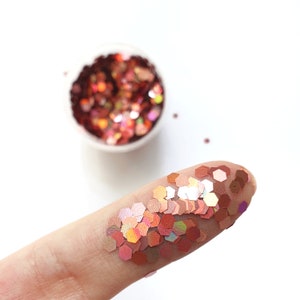 May include: A close-up of iridescent copper glitter in a hexagonal shape. The glitter is shown on a fingertip and in a small bowl.