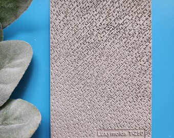 May include: A rectangular, light gray mold with a textured surface of small, irregular holes. The mold has a diagonal pattern and the text "Luxymolds T-250" is printed at the bottom. The background is a bright blue.