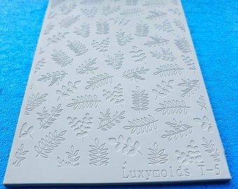 Pode incluir: Um molde de silicone branco com um design de várias formas de folhas. O molde é etiquetado como "Luxymolds T-5".