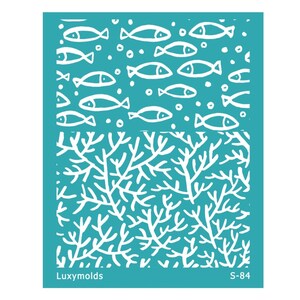 Può includere: Uno stencil turchese con un tema marino. La sezione superiore presenta un motivo di pesci bianchi e bolle. La sezione inferiore mostra un design di barriera corallina bianca. I testi "Luxymolds" e "S-84" sono visibili.