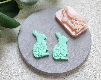 May include: Two light green polymer clay bunny shapes with floral designs, and a pink polymer clay mold of a bunny with floral designs.