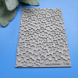 Puede incluir: Molde de silicona gris con un patrón repetitivo de pequeñas flores. El molde está etiquetado como "Luxymolds T-36".
