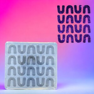 Op de afbeelding: Een transparante siliconen mal met 24 individuele mallen in de vorm van bogen. De mal bevindt zich op een roze en blauwe gradiënt achtergrond.