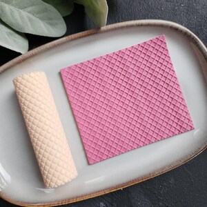 May include: Two silicone molds for baking, one is a flat square with a waffle pattern and the other is a cylinder with a waffle pattern. Both molds are pink and beige.