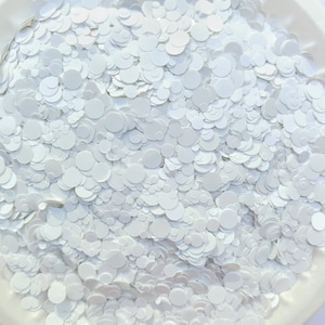 Op de afbeelding: Een close-up afbeelding van witte glitterconfetti. De confetti is gemaakt van kleine, ronde stukjes witte glitter.