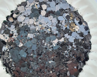 May include: A close-up of black, gray, and silver glitter. The glitter is in a variety of shapes and sizes.