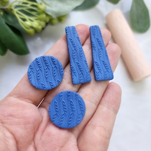 Op de afbeelding: Een set van vier blauwe polymer clay oorbellen met een tarwemotief. De oorbellen zijn in de vorm van twee cirkels en twee rechthoeken.