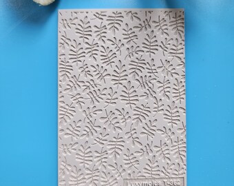 Pode incluir: Um molde de silicone cinza com um padrão repetitivo de pequenas folhas. O molde é etiquetado como "Luxymolds T-363".