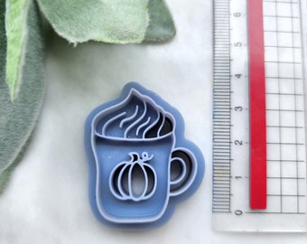 May include: A blue plastic cookie cutter shaped like a coffee mug with whipped cream and a pumpkin on the side.