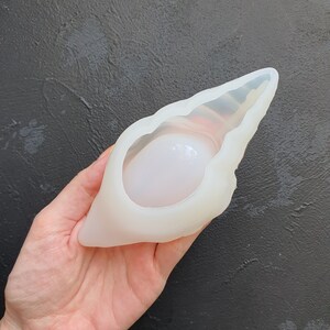 May include: White silicone mold shaped like a seashell with a smooth, rounded interior. The mold is designed for creating resin crafts.